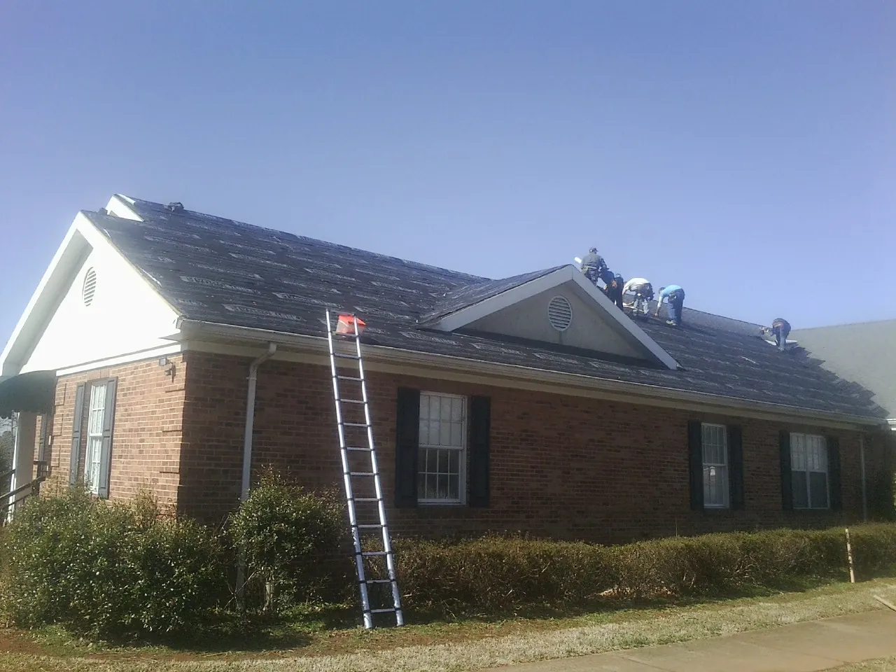 Crew tearing shingles off a brick ranch roof with a ladder set — Metal Roof Repair work by our crew in Billerica