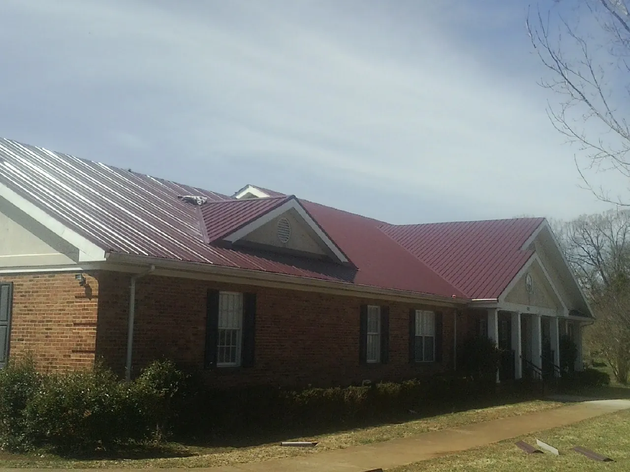 Red metal roof with gabled entries on a long brick building, from a Hail Damage Roof Repair job in Billerica