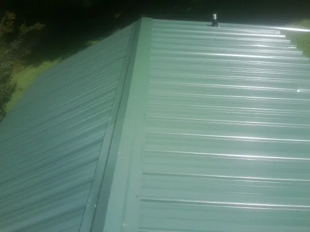 New green metal panels meeting at the ridge of a roof — Flat Roof Repair work by our crew in Billerica