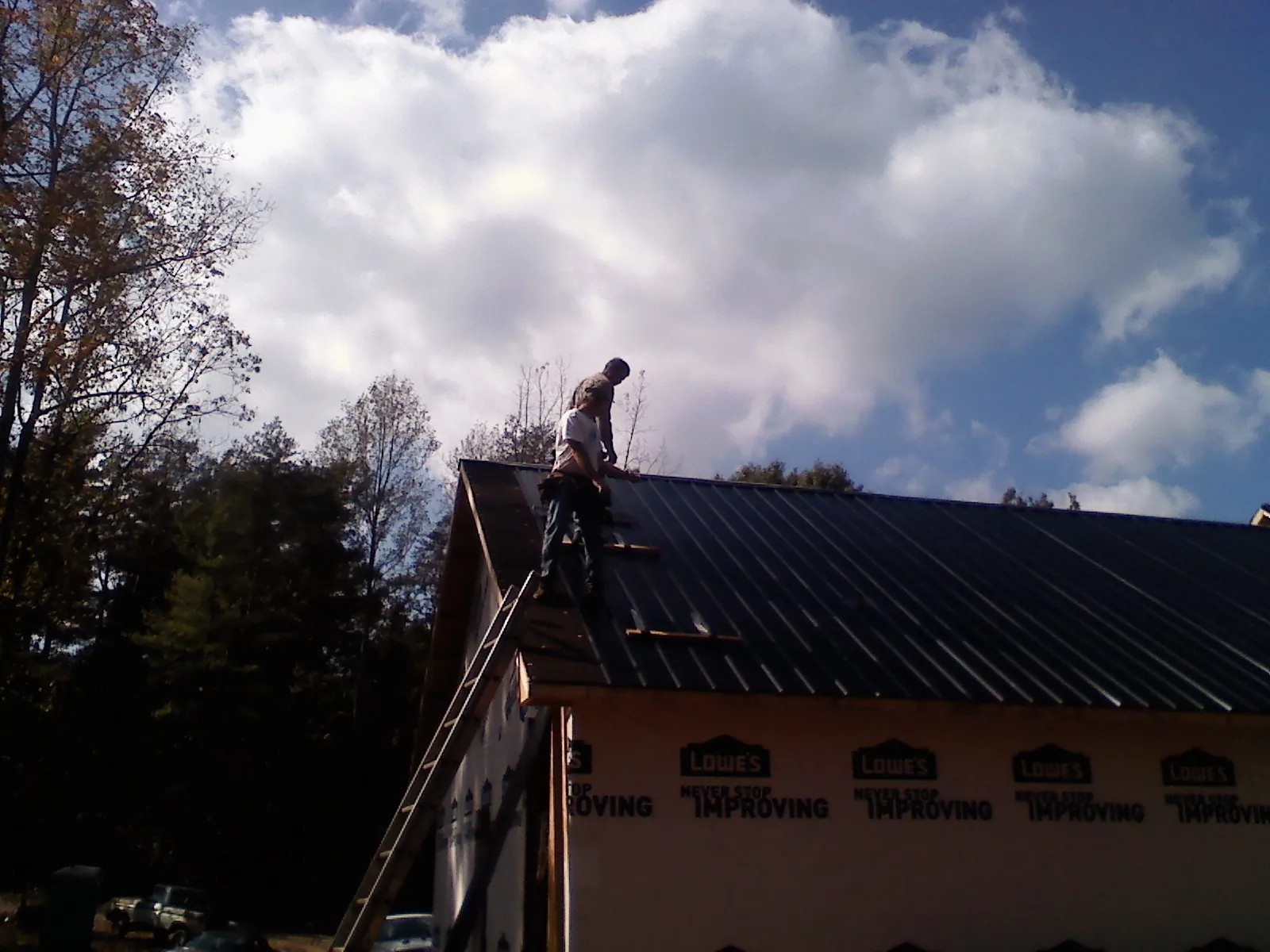 Roofer fastening dark metal panels high against a cloudy sky, from a Roof Inspection job in Billerica