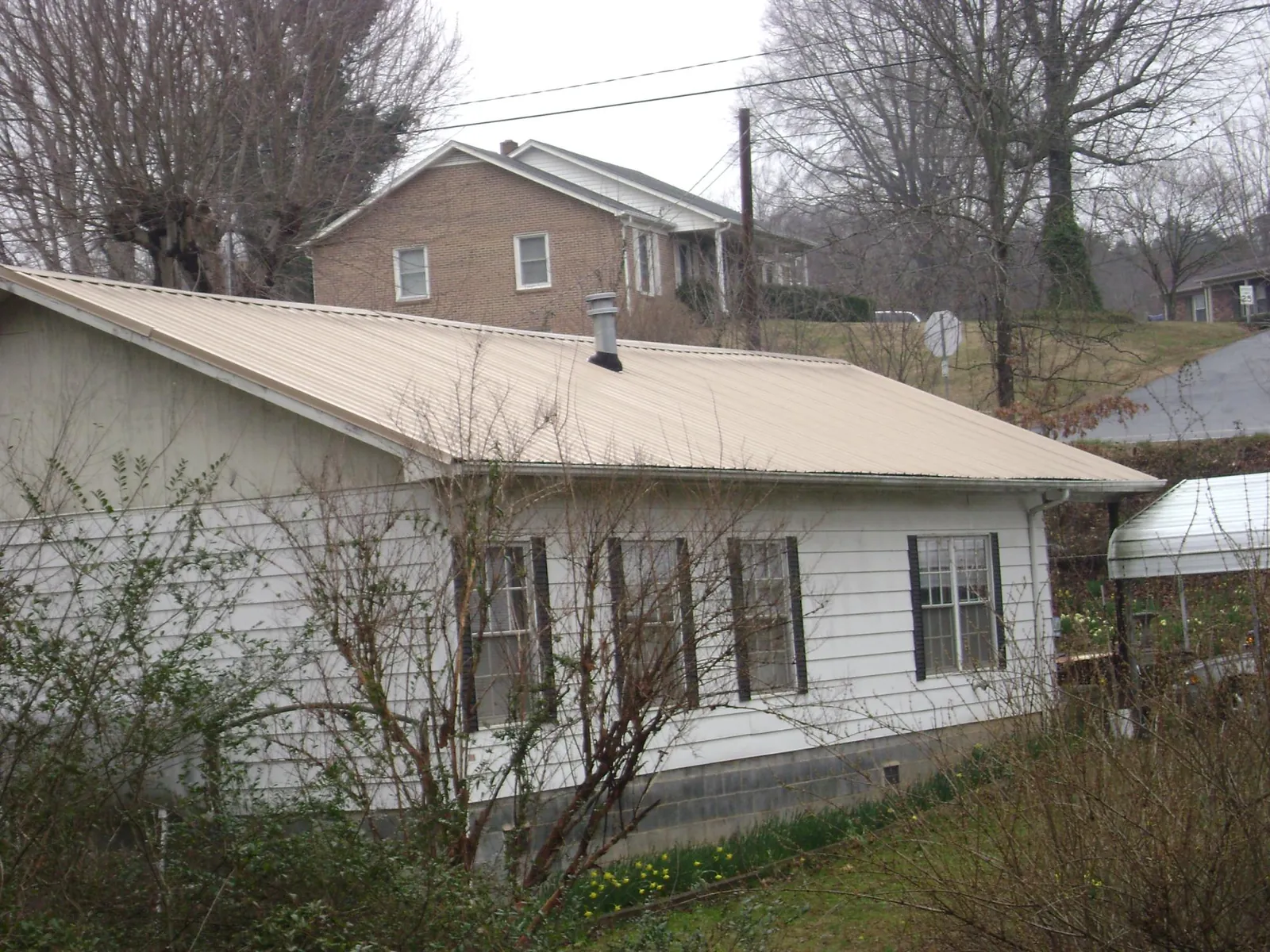 Tan metal roof on a white sided house set into a hillside — Commercial Roofing by Roofing Brothers in Billerica